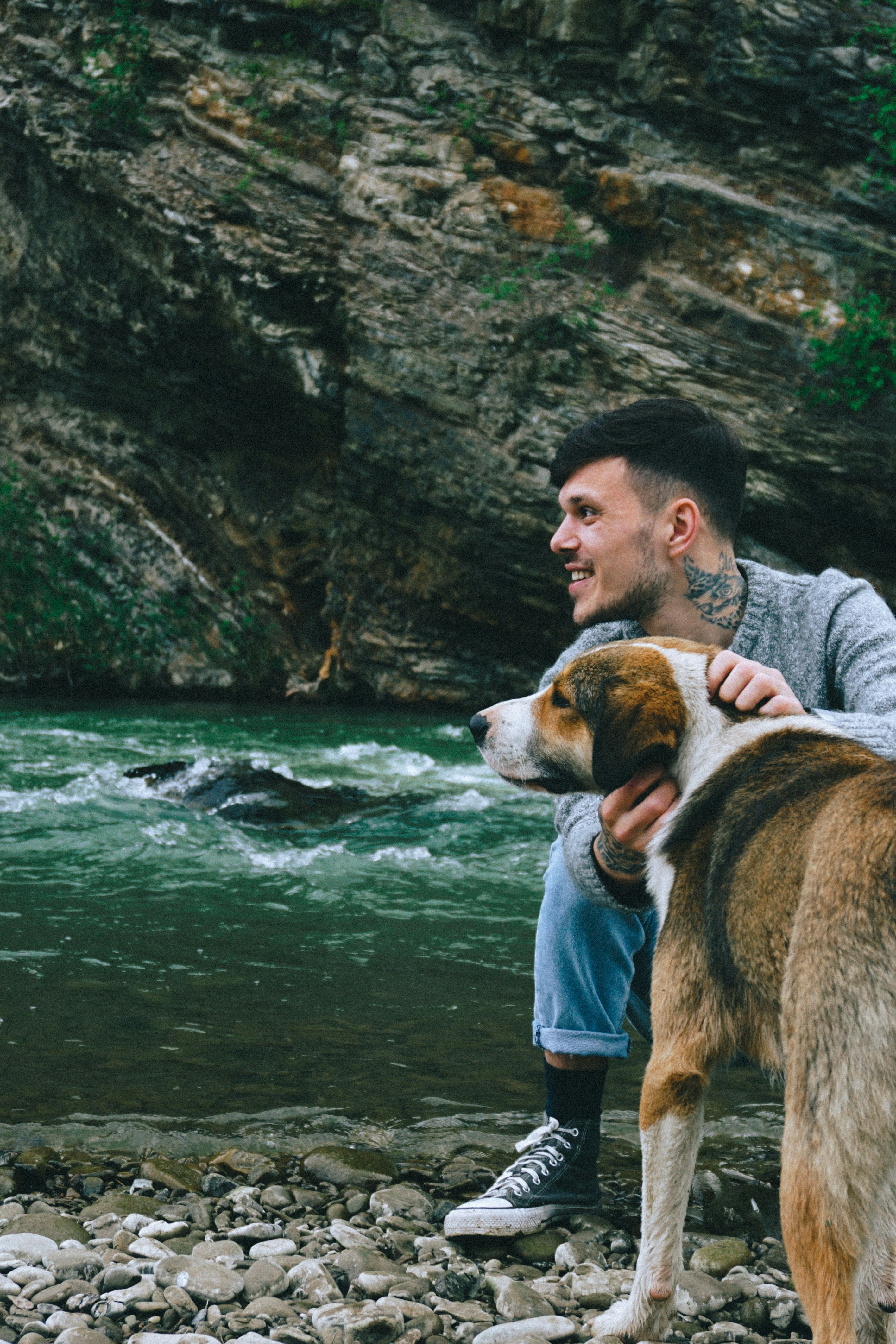 man in blue denim jacket holding brown and white dog on water during daytime